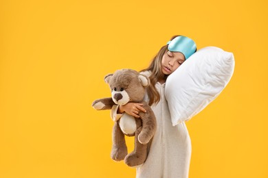 Photo of Overslept girl with sleep mask, pillow and teddy bear on orange background, space for text