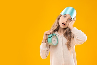 Photo of Overslept girl with sleep mask and alarm clock on orange background, space for text