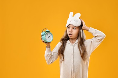 Overslept girl with sleep mask and alarm clock on orange background, space for text