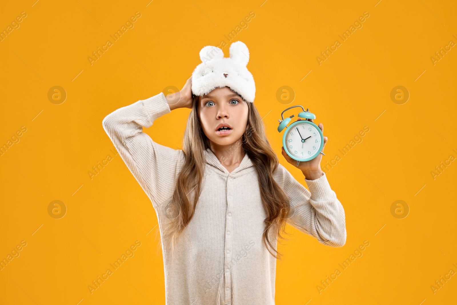 Photo of Overslept girl with sleep mask and alarm clock on orange background