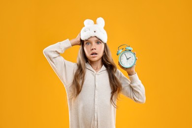 Overslept girl with sleep mask and alarm clock on orange background