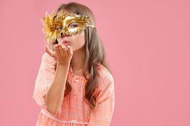 Cute girl wearing carnival mask and blowing kiss on pink background, space for text