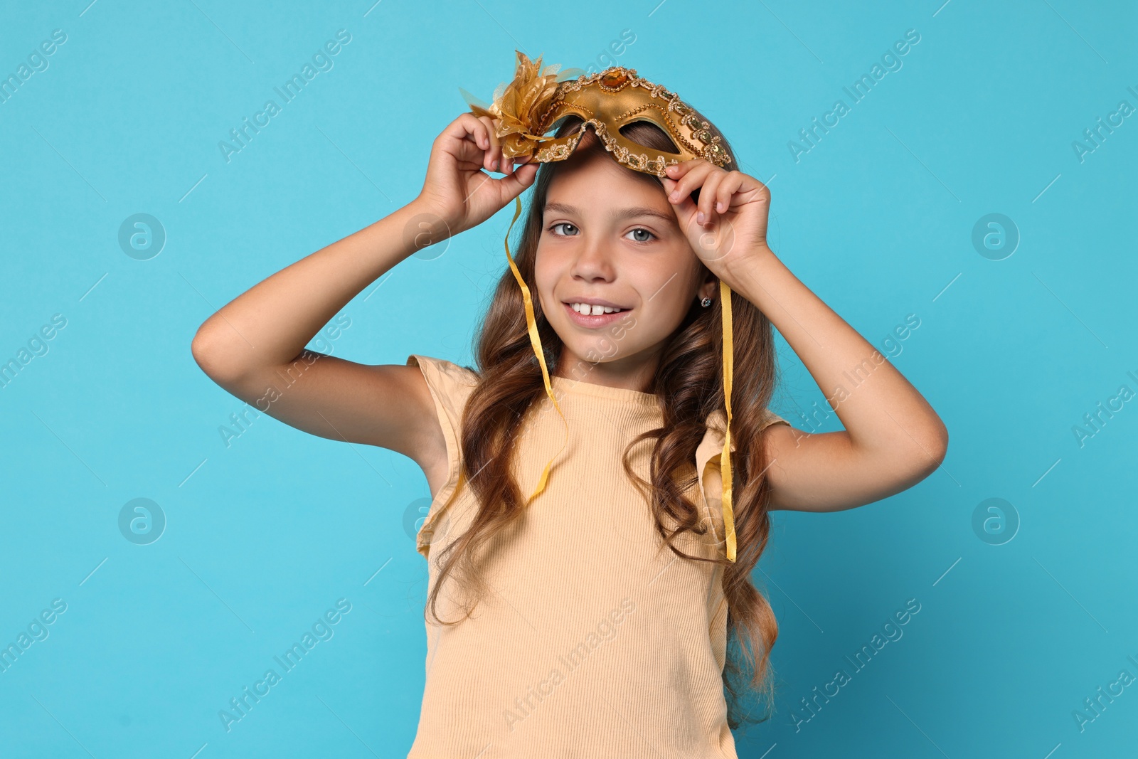 Photo of Happy girl wearing carnival mask on light blue background