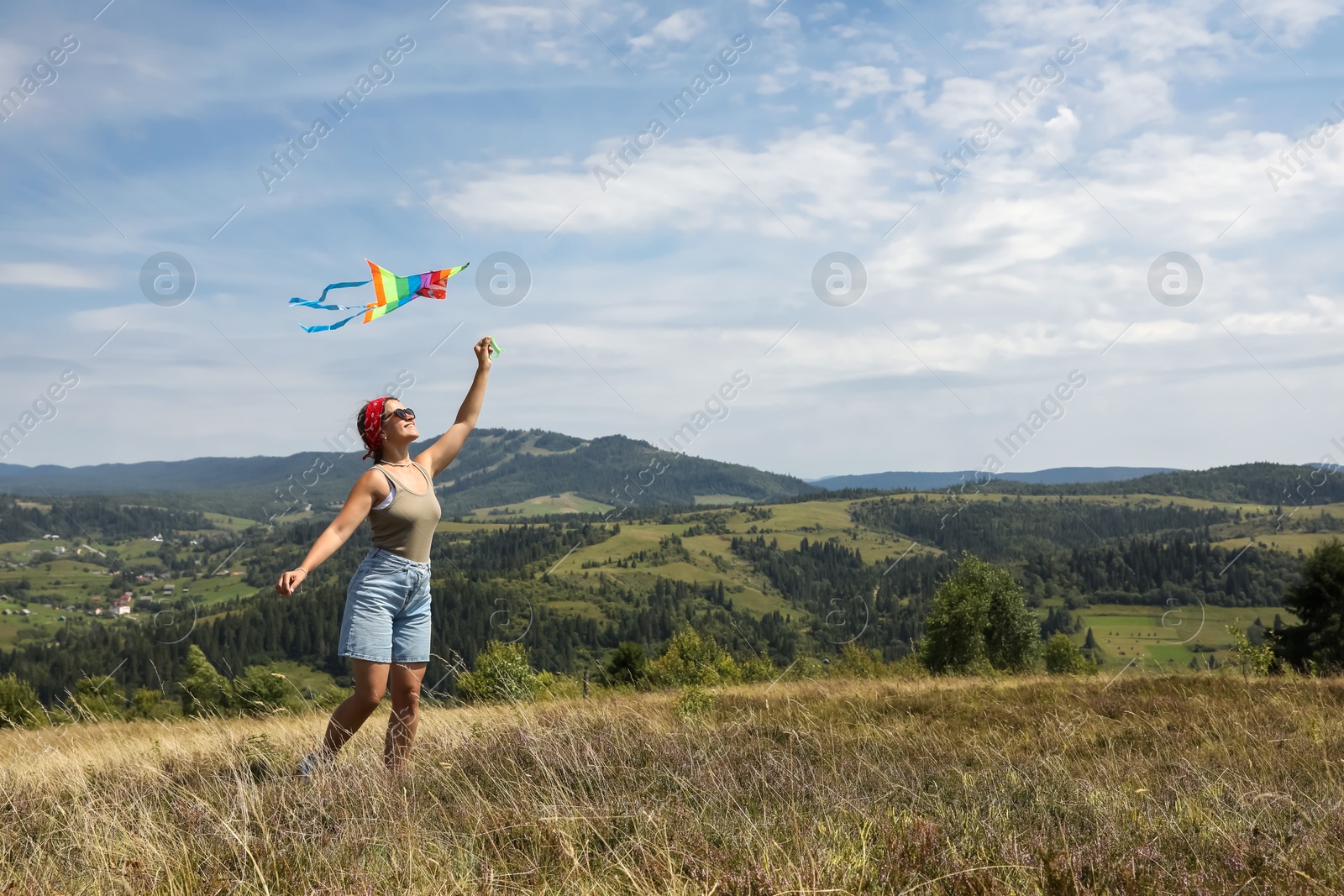 Photo of Smiling woman flying kite at field under blue sky. Space for text