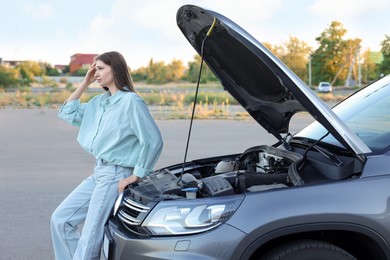 Photo of Stressed woman standing near broken car outdoors