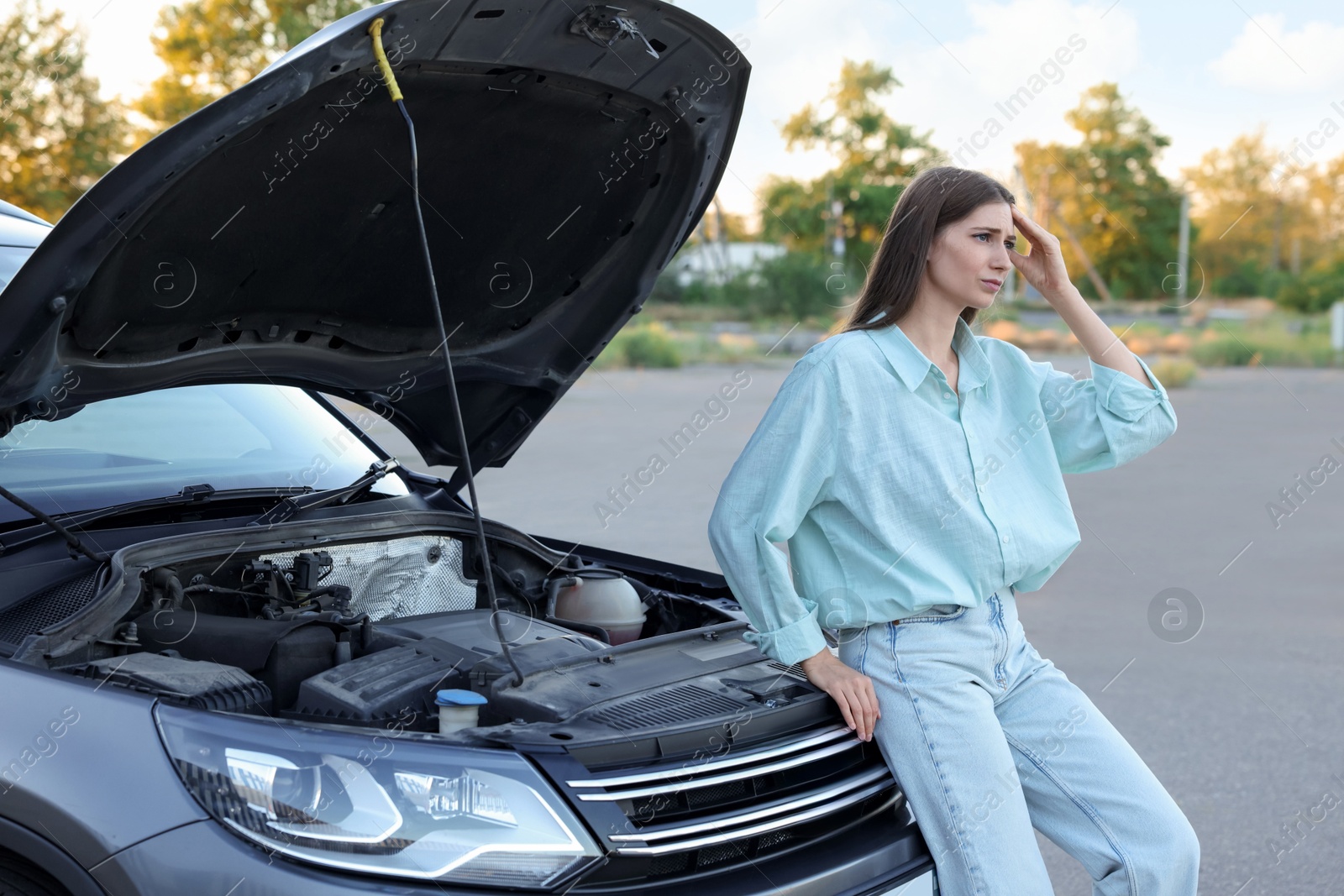 Photo of Stressed woman standing near broken car outdoors