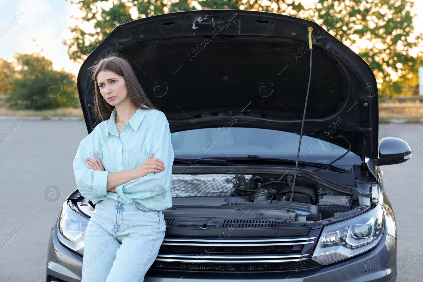 Photo of Stressed woman standing near broken car outdoors