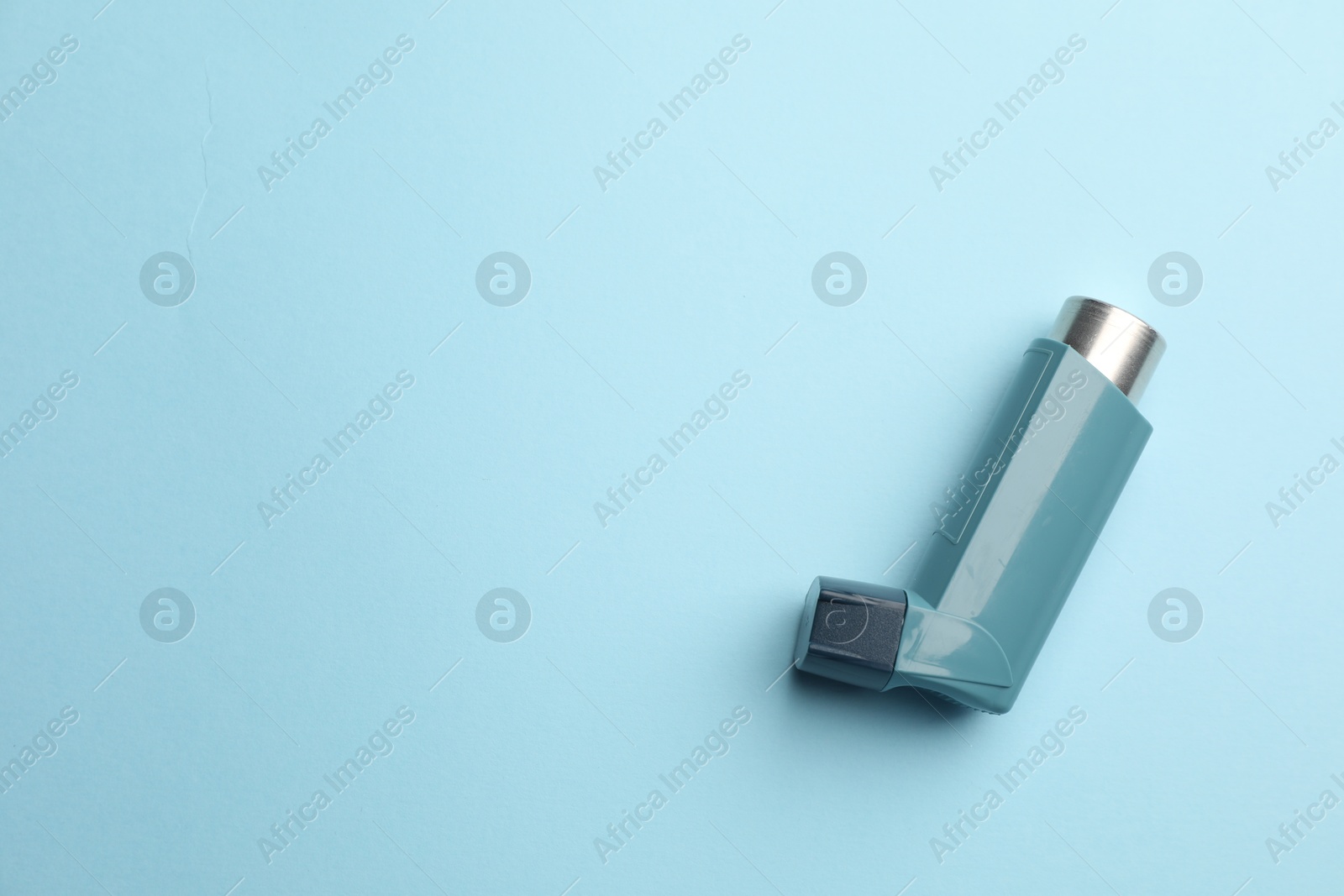 Photo of Asthma inhaler on light blue background, top view. Space for text