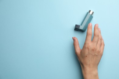 Photo of Woman holding asthma inhaler on light blue background, top view. Space for text