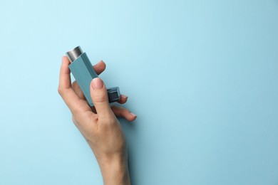 Photo of Woman holding asthma inhaler on light blue background, top view. Space for text