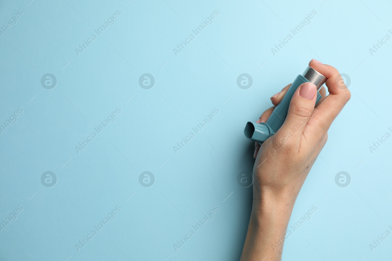 Photo of Woman holding asthma inhaler on light blue background, top view. Space for text