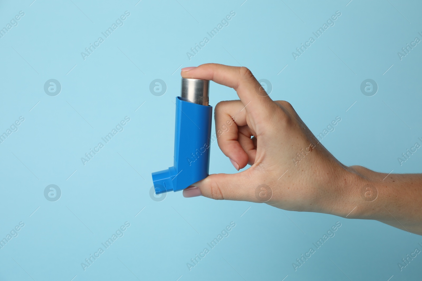 Photo of Woman holding asthma inhaler on light blue background, closeup