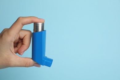 Woman holding asthma inhaler on light blue background, closeup. Space for text