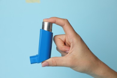 Woman holding asthma inhaler on light blue background, closeup