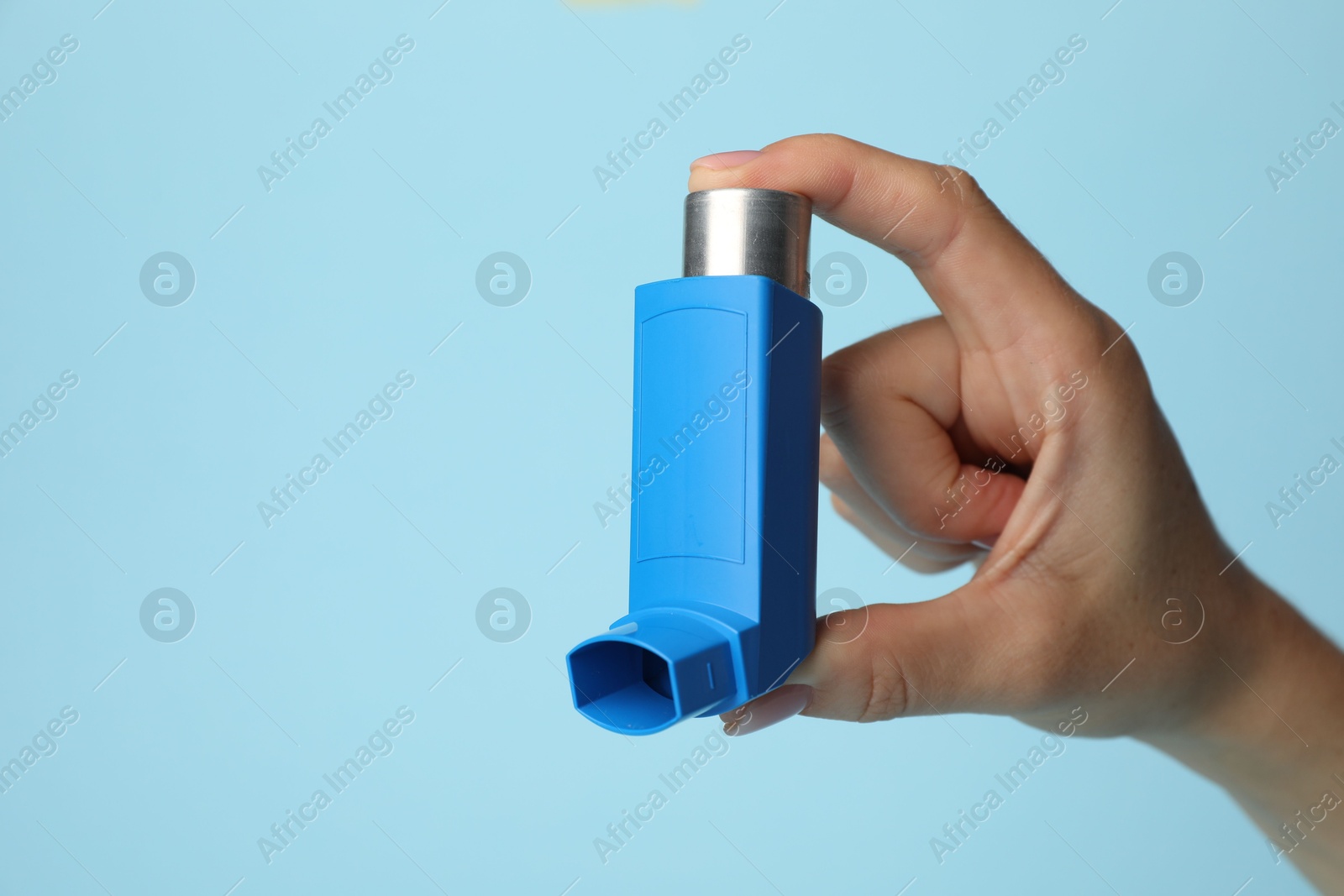 Photo of Woman holding asthma inhaler on light blue background, closeup. Space for text