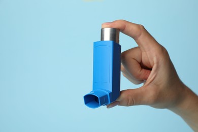 Woman holding asthma inhaler on light blue background, closeup. Space for text