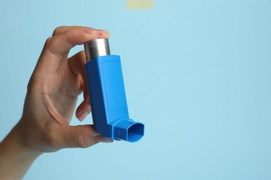 Photo of Woman holding asthma inhaler on light blue background, closeup. Space for text