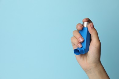 Photo of Woman holding asthma inhaler on light blue background, closeup. Space for text