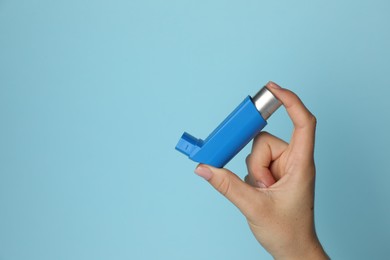 Photo of Woman holding asthma inhaler on light blue background, closeup. Space for text