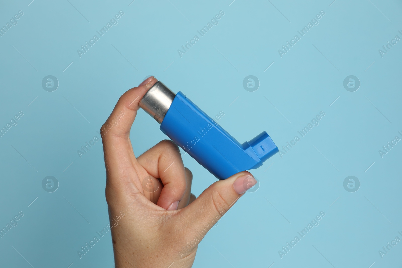 Photo of Woman holding asthma inhaler on light blue background, closeup