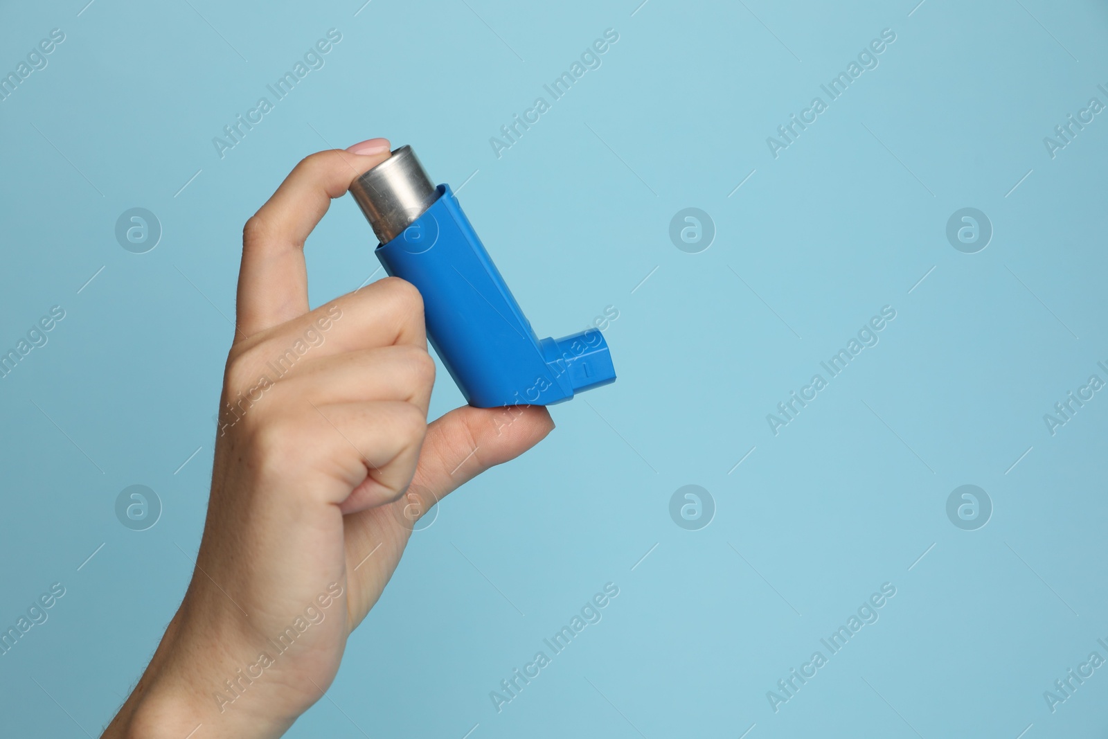 Photo of Woman holding asthma inhaler on light blue background, closeup. Space for text