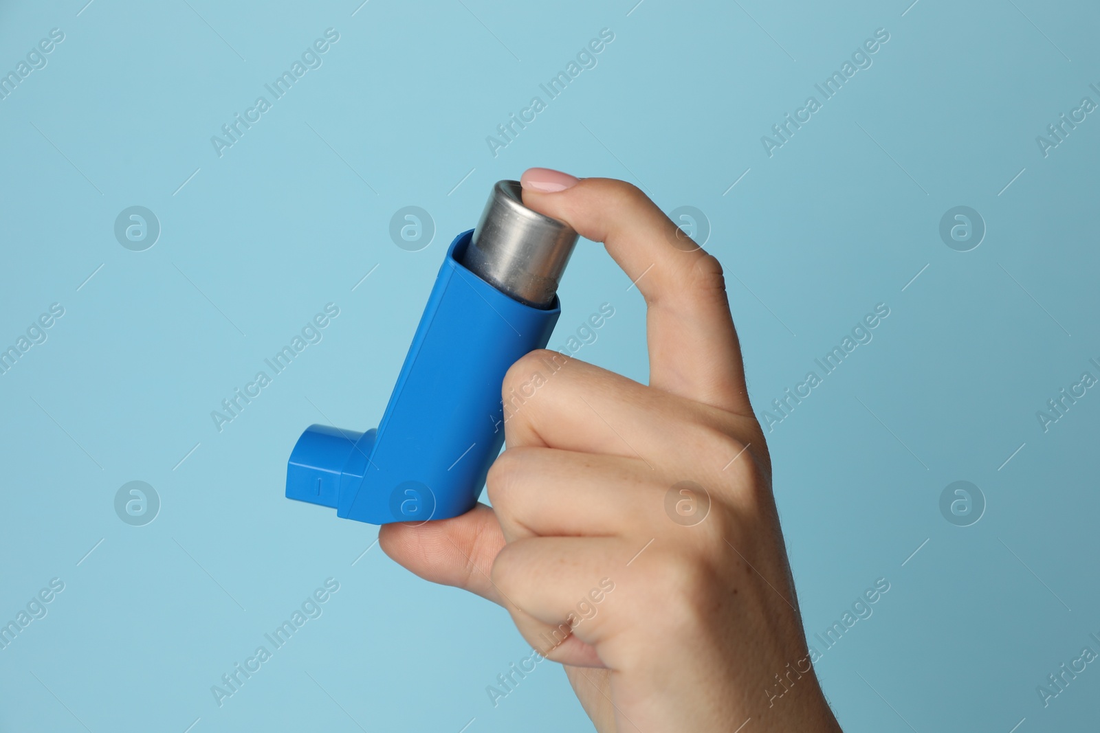 Photo of Woman holding asthma inhaler on light blue background, closeup