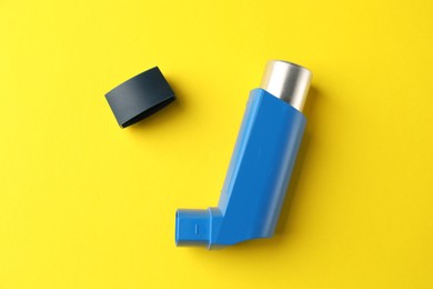 Asthma inhaler on yellow background, top view