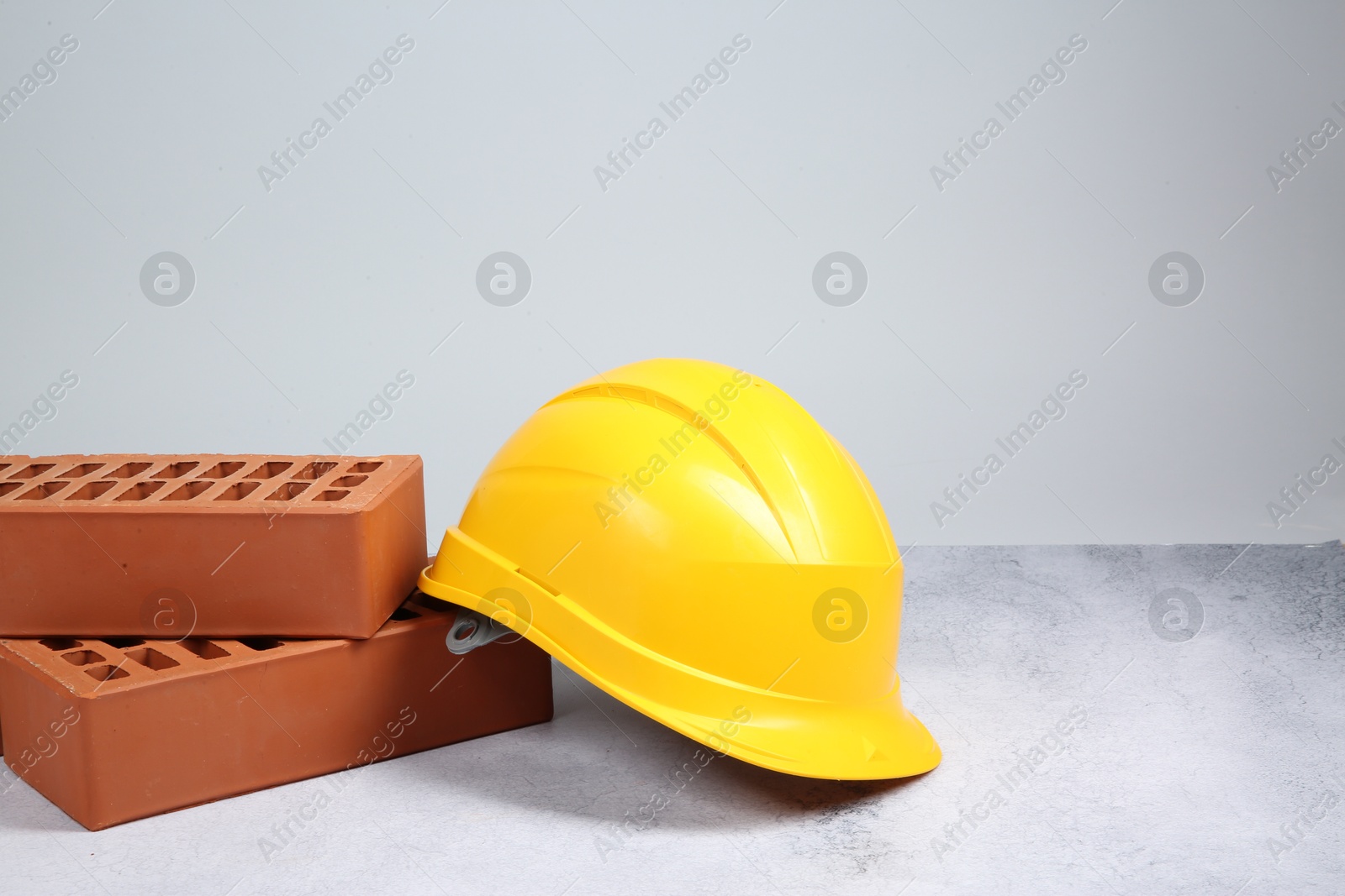 Photo of Red bricks and hard hat on textured table against light background. Space for text