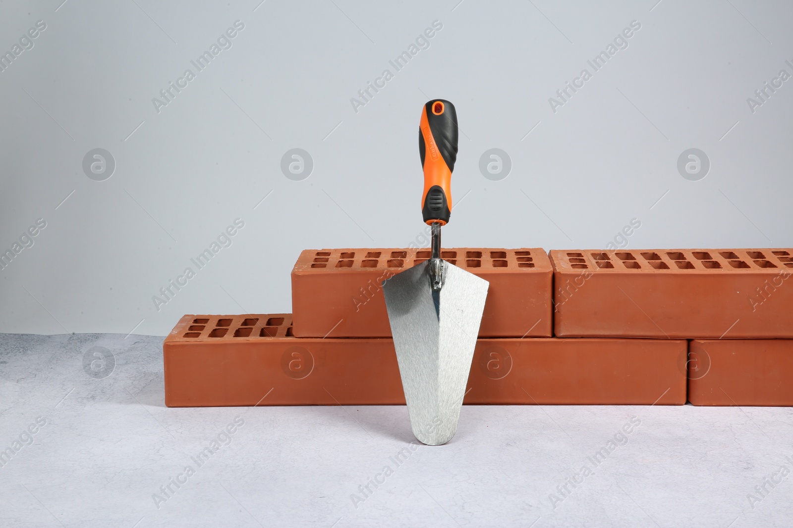 Photo of Red bricks and trowel on textured table against light background. Building material