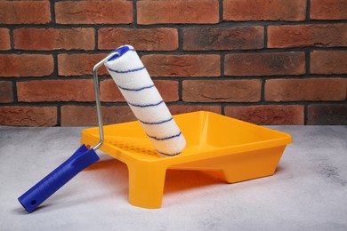 Paint roller and yellow tray on light textured table against red brick wall