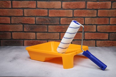 Paint roller and yellow tray on light textured table against red brick wall