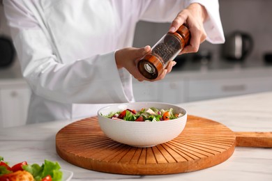 Photo of Professional chef adding pepper to delicious salad at white marble table in kitchen, closeup