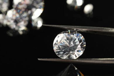 Photo of Tweezers with beautiful shiny diamond on black mirror surface, closeup