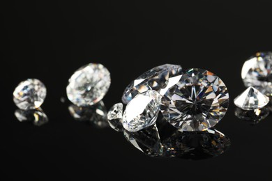 Photo of Many beautiful shiny diamonds on black mirror surface, closeup