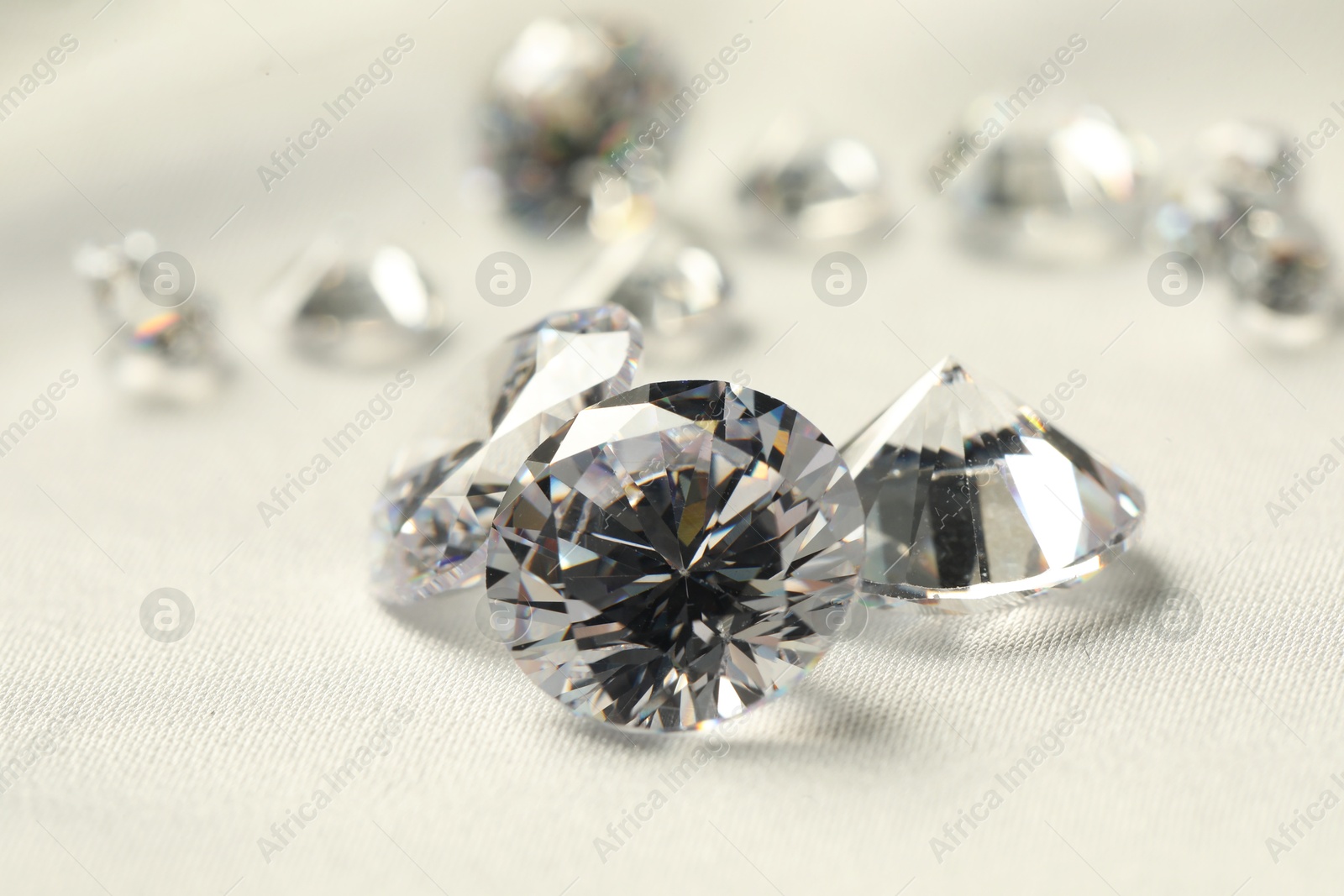 Photo of Many beautiful shiny diamonds on white fabric, closeup