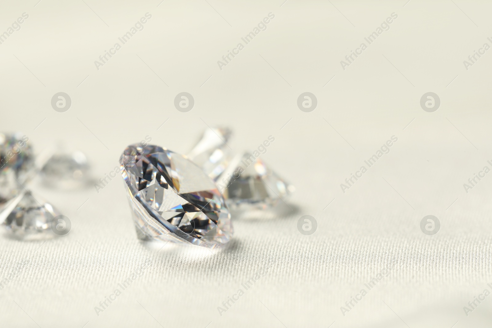 Photo of Many beautiful shiny diamonds on white fabric, closeup. Space for text