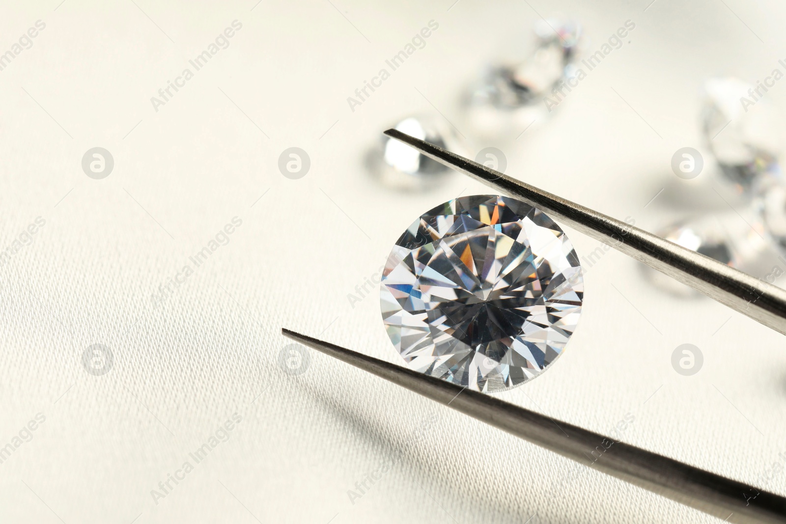 Photo of Tweezers with beautiful shiny diamonds on white fabric, closeup. Space for text