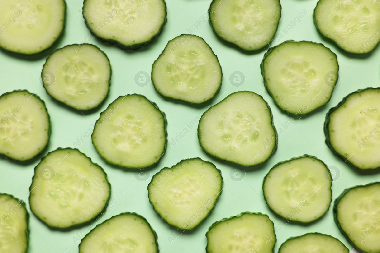 Photo of Slices of fresh cucumbers on turquoise background, flat lay