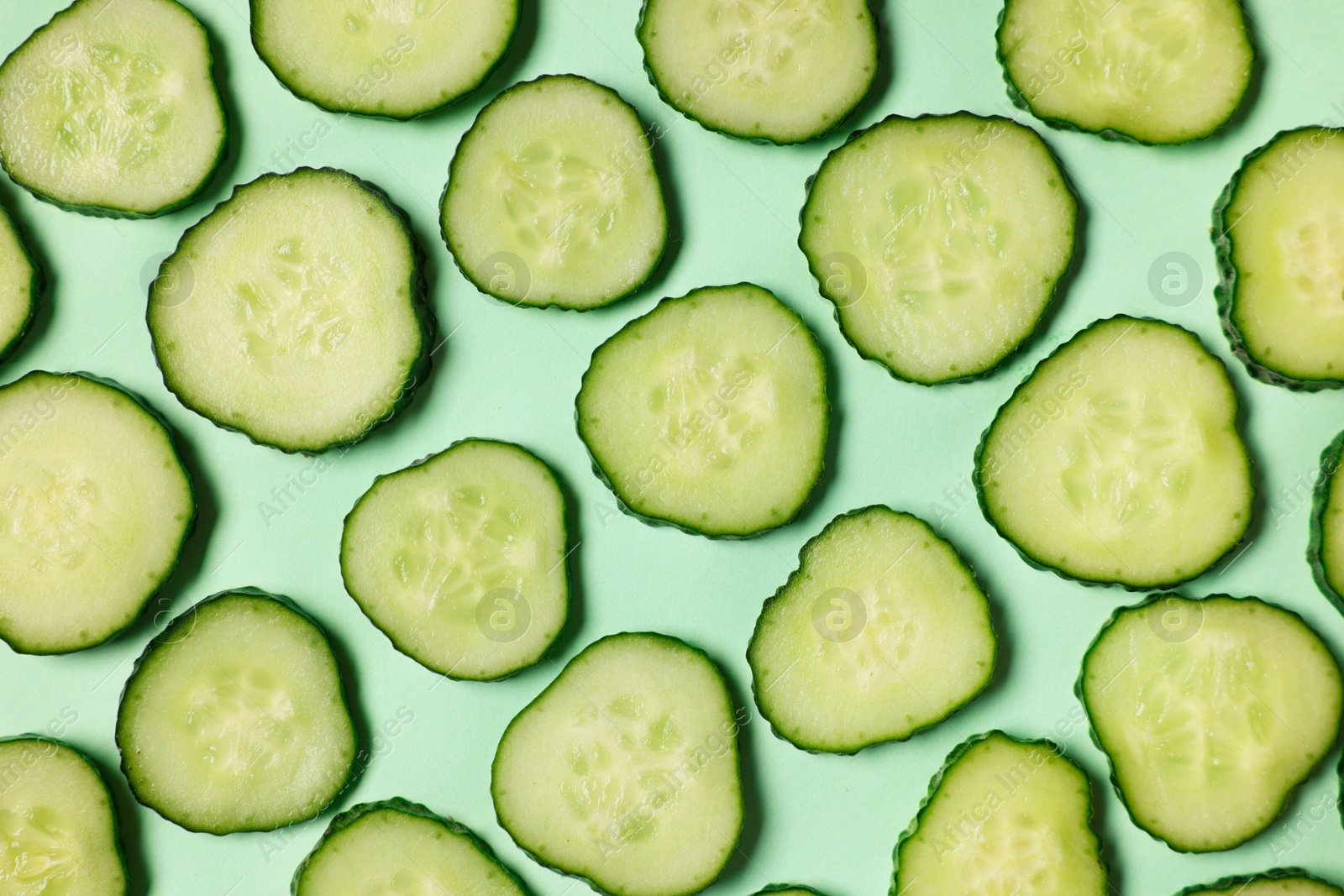 Photo of Slices of fresh cucumbers on turquoise background, flat lay