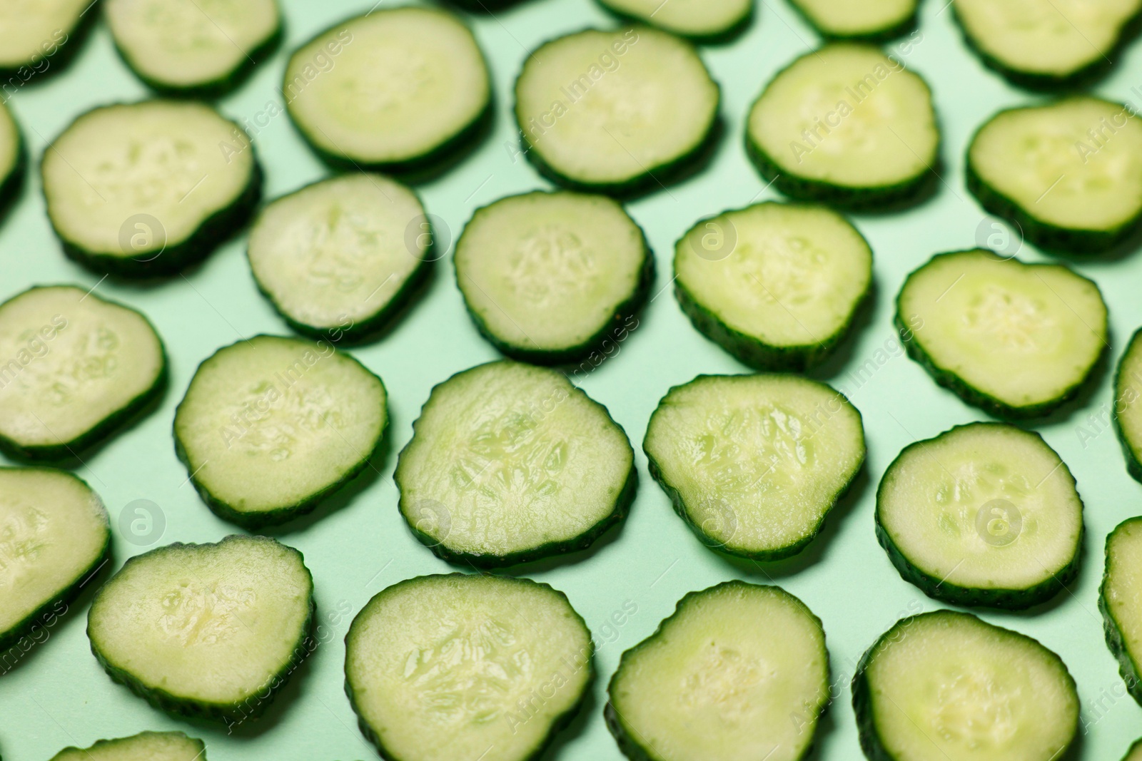 Photo of Slices of fresh cucumbers on turquoise background, above view