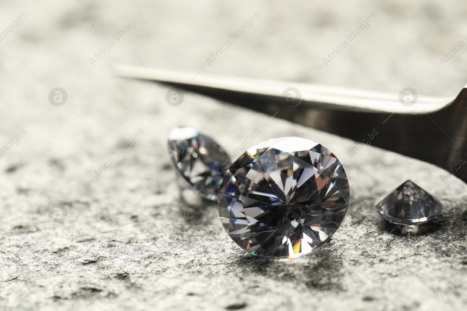 Photo of Many beautiful shiny diamonds and tweezers on grey textured table, closeup. Space for text