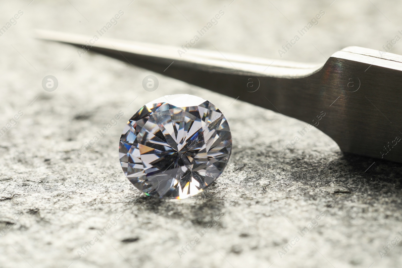 Photo of Beautiful shiny diamond and tweezers on grey textured table, closeup