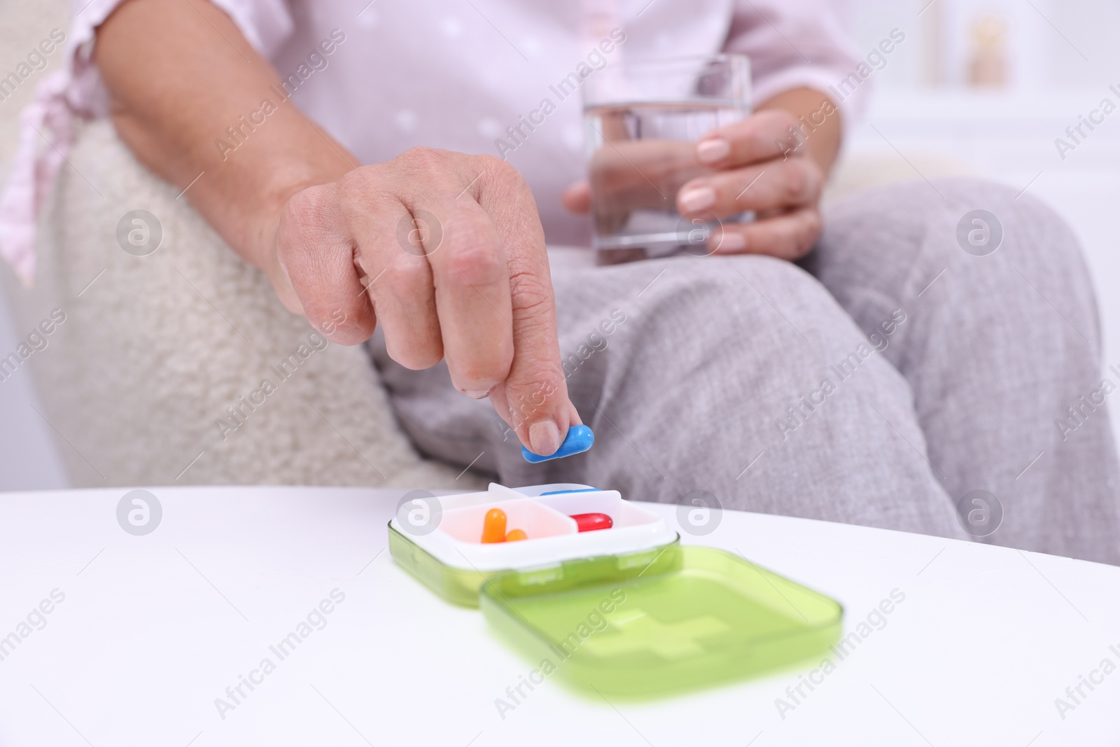 Photo of Senior woman taking pill from organizer at home, closeup