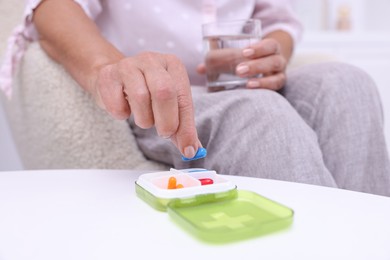 Photo of Senior woman taking pill from organizer at home, closeup