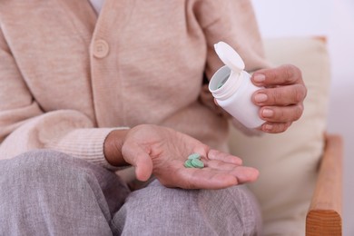 Photo of Senior man pouring pills from bottle into hand at home, closeup