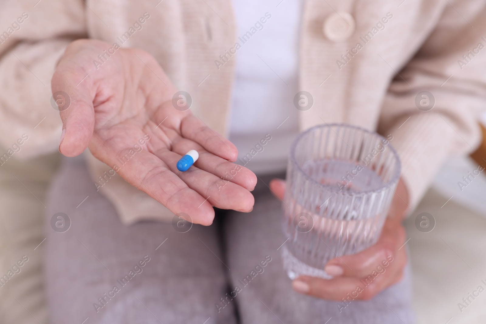 Photo of Senior woman with pill and glass of water at home, closeup