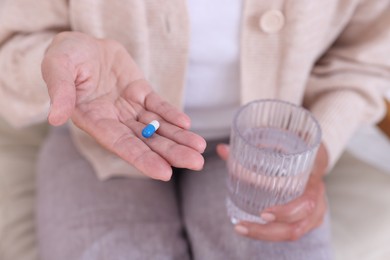 Senior woman with pill and glass of water at home, closeup