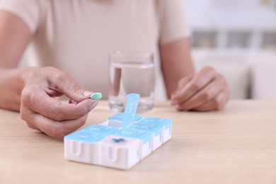 Photo of Senior woman taking pill from organizer at table indoors, closeup