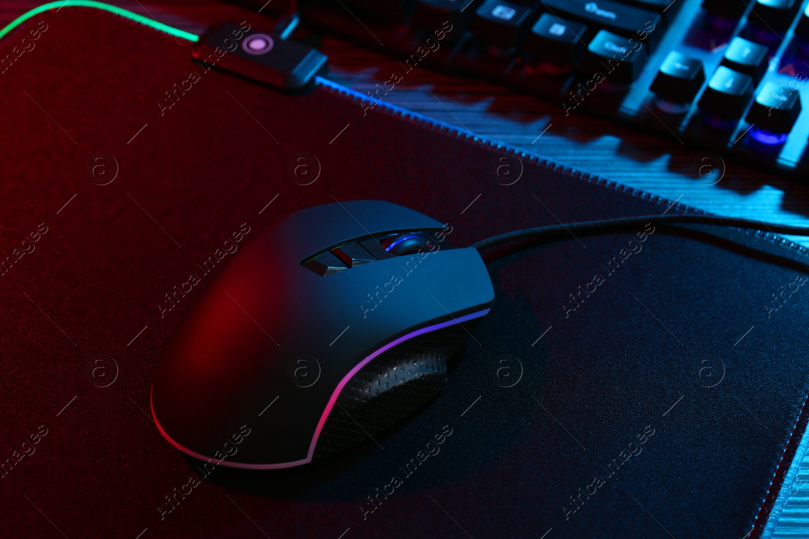 Photo of Computer mouse and mousepad on table in neon lights, closeup