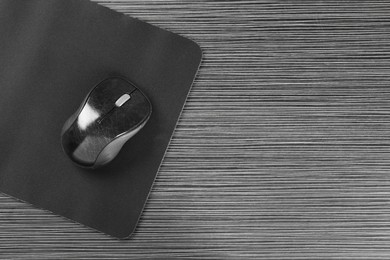 Photo of Computer mouse with mousepad on black wooden table, top view. Space for text